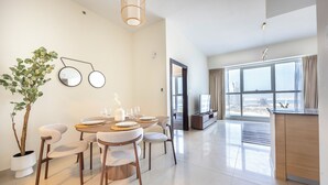 A modern living room with a dining area, large windows, and a view of the city. - Bloomfields 1BR in Marina Bay 1  (Abu Dhabi)