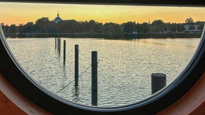 Une fenêtre circulaire offrant une vue sur une étendue d’eau calme, une côte lointaine et un ciel dégagé.