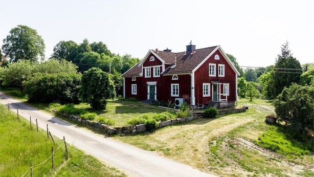 Ein rotes Haus mit geneigtem Dach, einer Veranda und einer Auffahrt zum Eingang.
