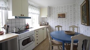Eine Küche mit Herd, Backofen und Schränken, einem Esstisch mit Stühlen und Wandpapier mit Muster.