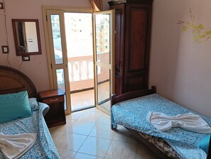 A bedroom with two beds, a wooden wardrobe, a mirror, and a sliding door to a balcony. - The Tent (Marsa Matrouh)