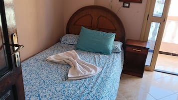 Cama bem arrumada com roupa de cama estampada, cabeceira de madeira, mesa de cabeceira e um espelho na parede.