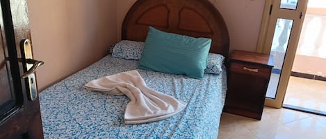 A neatly made bed with patterned bedding, a wooden headboard, a bedside table, and a mirror on the wall.