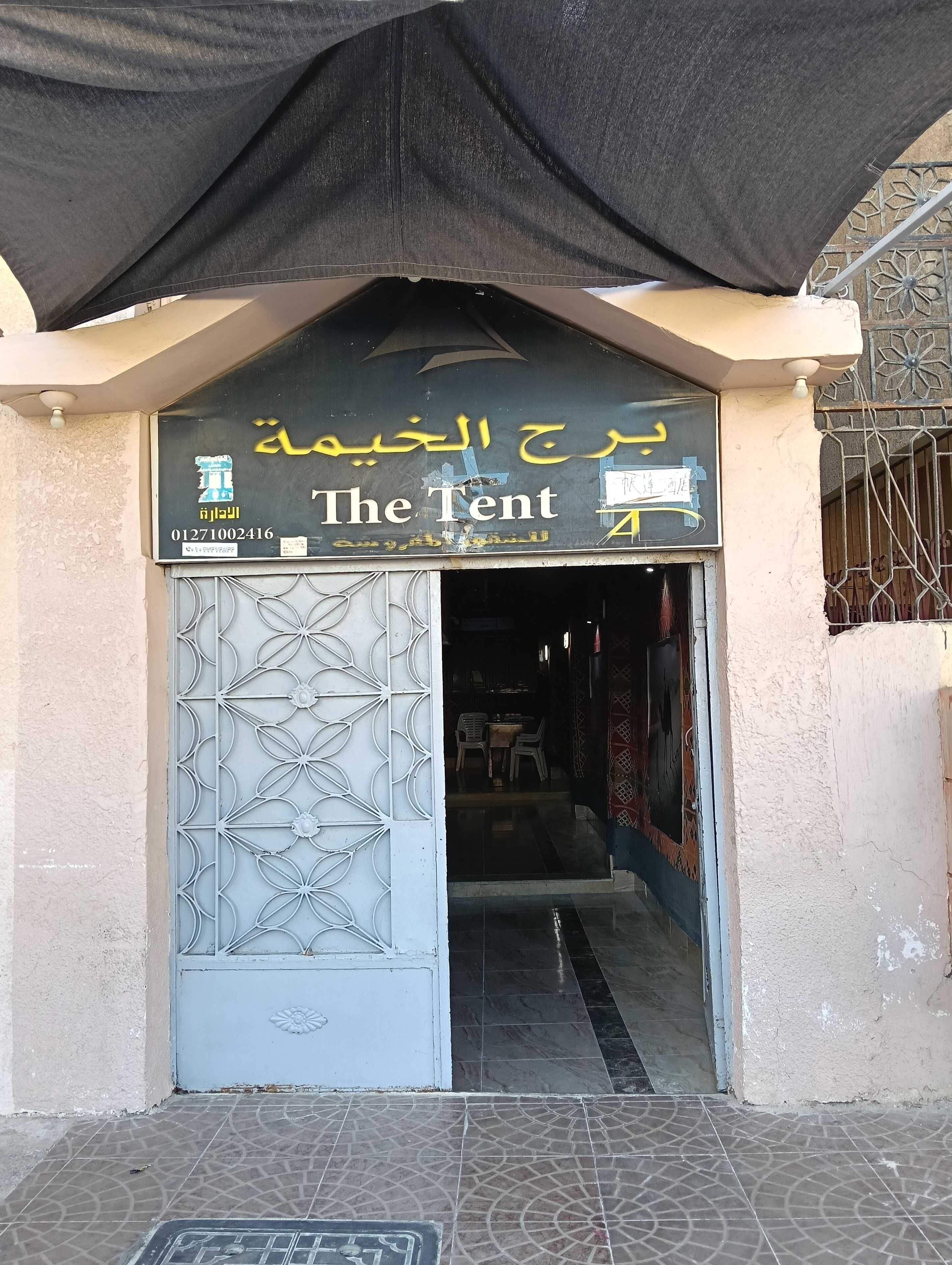 Ein Gebäudeeingang mit einem Schild, auf dem 'The Tent' steht, und darüber arabische Schriftzeichen.