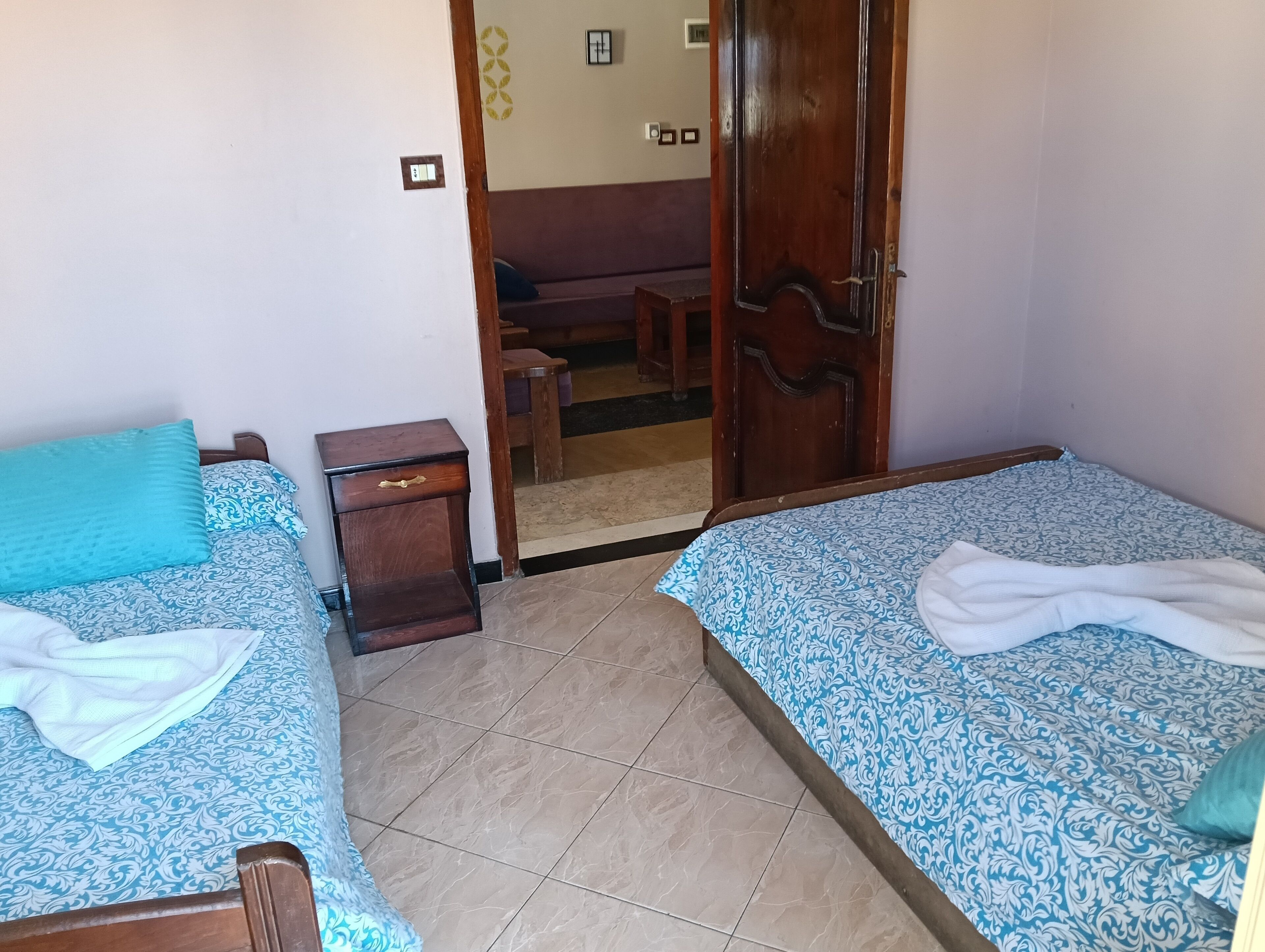 Une chambre avec deux lits, une table de chevet en bois et une porte donnant sur un coin salon.