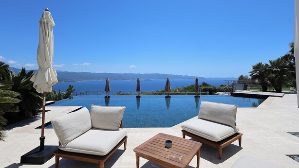 En infinitypool med utsikt över havet, två solstolar, ett bord och parasoller.