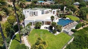 Ett modernt hus med en swimmingpool, omgivet av frodig grönska och med ett bergigt landskap i bakgrunden.