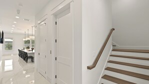 Een modern interieur met een trap, witte muren en een eethoek met stoelen en een tafel.