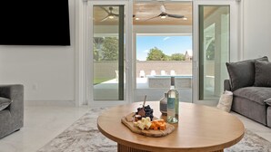 Een moderne woonkamer met een ronde houten salontafel, een flatscreen-televisie aan de muur bevestigd en een schuifpui naar een buitengebied.