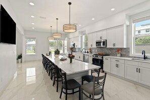 A modern kitchen with white cabinets, a large island, stainless steel appliances, and pendant lighting. - Sleeps 46 • Luxe Dune Allen Beach Group Stay • Pool + Spa | Satinwood Retreat (Santa Rosa Beach)