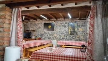 A rustic dining area with stone walls, wooden benches, and red and white checkered tablecloths.