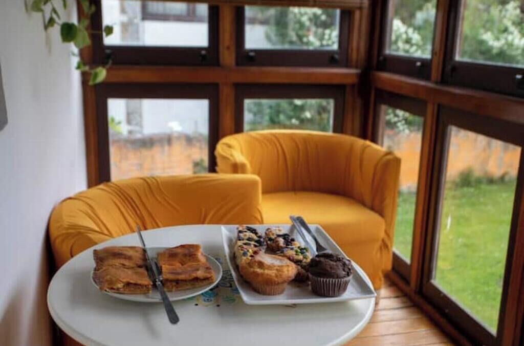 Una habitación con una mesa lista para el desayuno, un sillón amarillo y ventanas grandes.