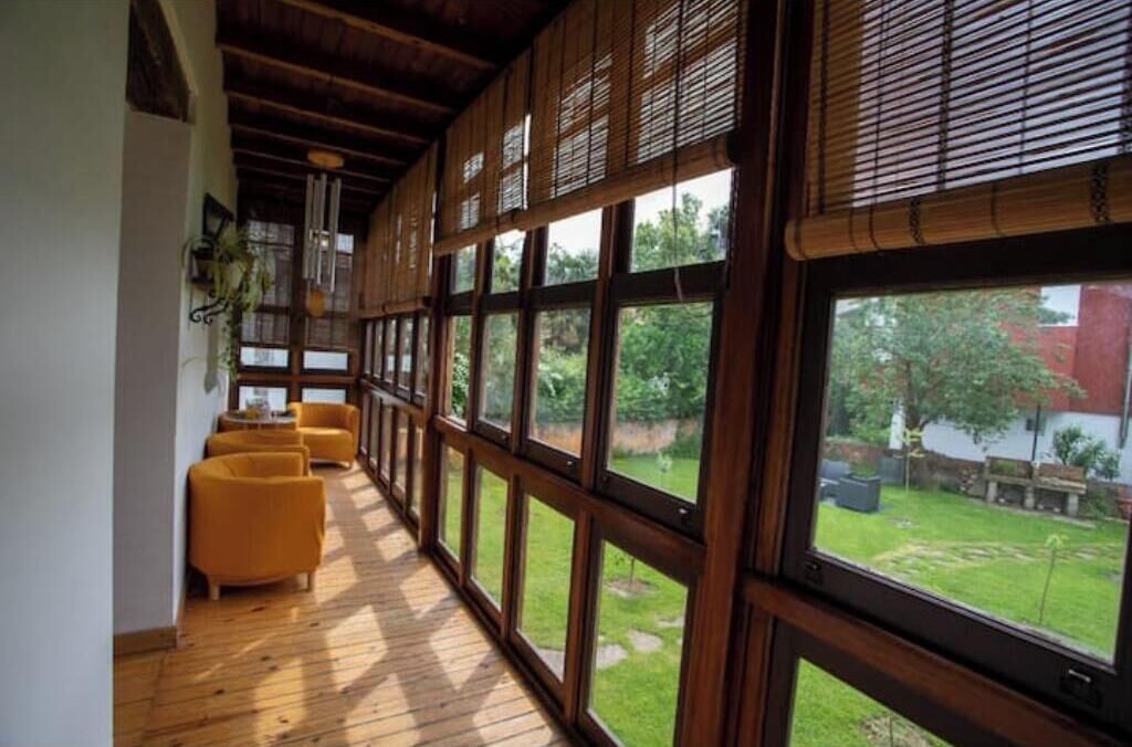 Un pasillo con piso de madera y ventanas amplias, que conduce a un jardín exterior.