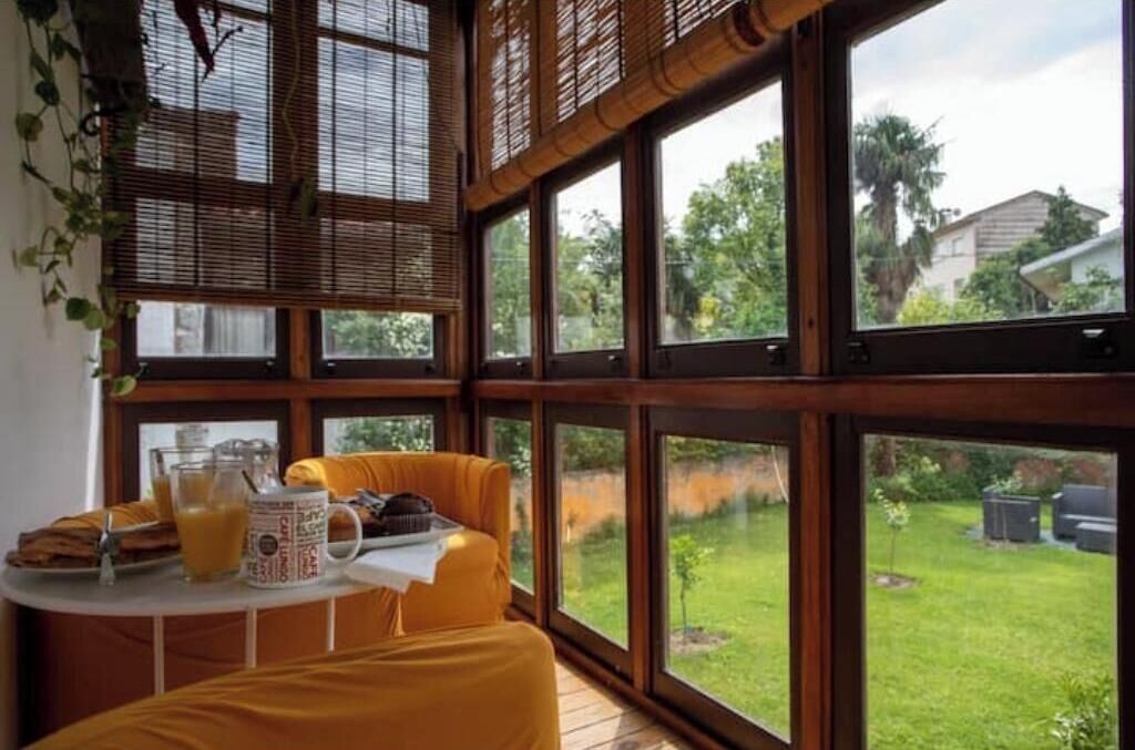 Una habitación con ventanas amplias, una mesa con alimentos para el desayuno y vista a un jardín.