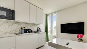 Eine moderne Küche mit weißen Schränken, einer Marmorarbeitsplatte, einer eingebauten Mikrowelle und einem großen Fenster mit grünen Vorhängen.