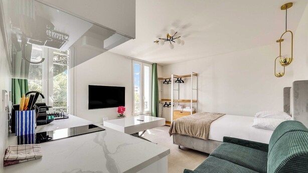 Ein modernes Hotelzimmer mit Bett, Sofa, Fernseher, Küchenzeile und Balkon.