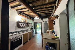 A kitchen with a stove, sink, and cabinets, a wooden ceiling, and a door leading outside. - Peaceful Country Retreat near Pesaro (Pesaro)