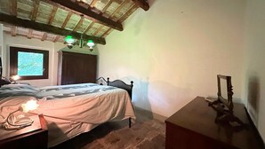 Une chambre à coucher avec un plafond en bois, un lit avec une tête de lit, une table de chevet avec une lampe et une fenêtre donnant sur un beau paysage.