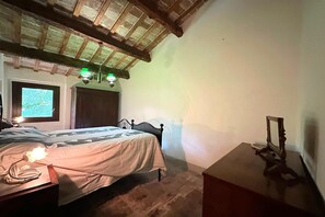 A bedroom with a wooden ceiling, a bed with a headboard, a bedside table with a lamp, and a window with a view. - Peaceful Country Retreat near Pesaro (Pesaro)