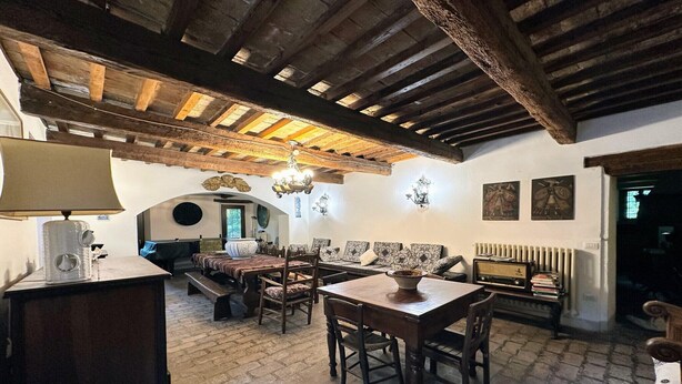 Un intérieur rustique avec des poutres apparentes, un sol en pierre, une table à manger avec des chaises, un canapé et un radiateur.