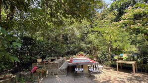 Une terrasse de jardin avec une table et des chaises, entourée de plantes en pot et d’arbres.