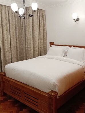 Un lit bien fait, avec du linge de lit blanc, une tête de lit en bois et un plancher en bois.