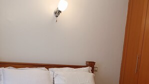 Una cama bien hecha con ropa blanca, un cabecero de madera y una lámpara fijada a la pared.