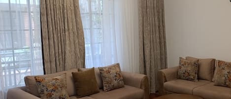 Uma sala de estar com sofá bege, almofadas florais, mesa de centro de madeira e um lustre.