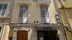 Ein Gebäude mit Café und Salon im Erdgeschoss, einer Holztür und mehreren Balkonen mit Rollläden.
