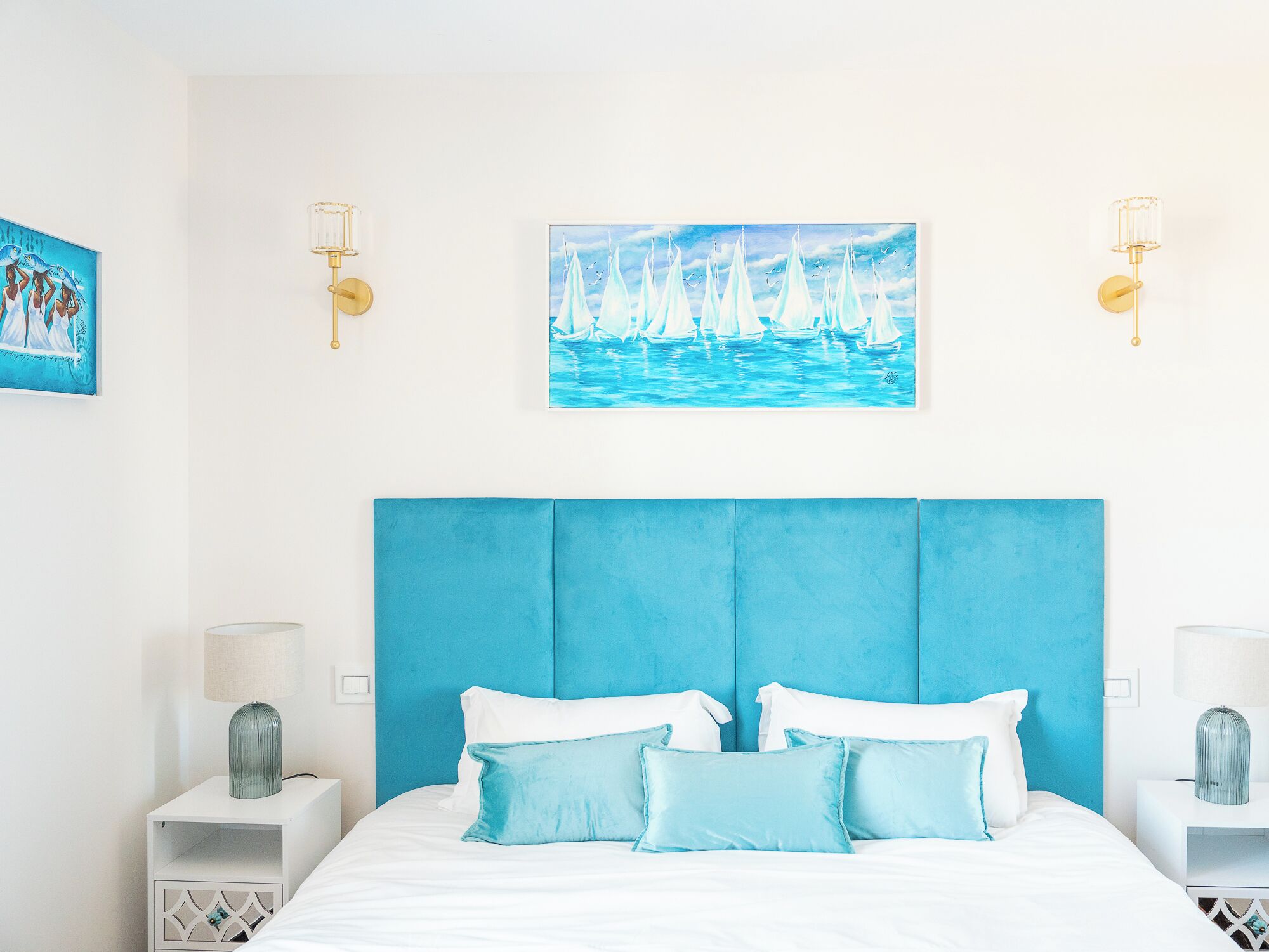 Een kamer met een groot bed, twee nachtkastjes en wanddecoratie met afbeeldingen van zeilboten.
