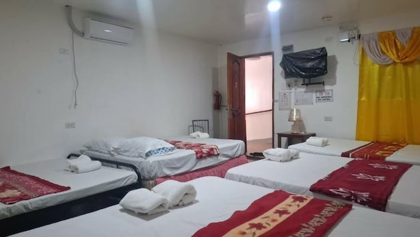 A hotel room with four beds, a wall-mounted air conditioner, a door leading to another room, and a small table with a lamp. - KNIGHT'S - APPLE INN (Mambajao)