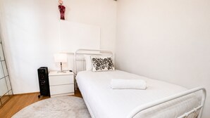 Une chambre avec un lit blanc, une table de chevet avec une lampe, un petit vase décoratif et un tapis rond posé sur un plancher en bois.