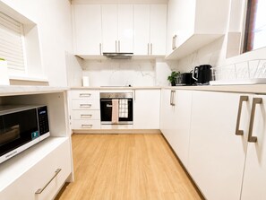 Eine moderne Küche mit weißen Schränken, einem Einbauofen, einer Mikrowelle und einer Kaffeemaschine.
