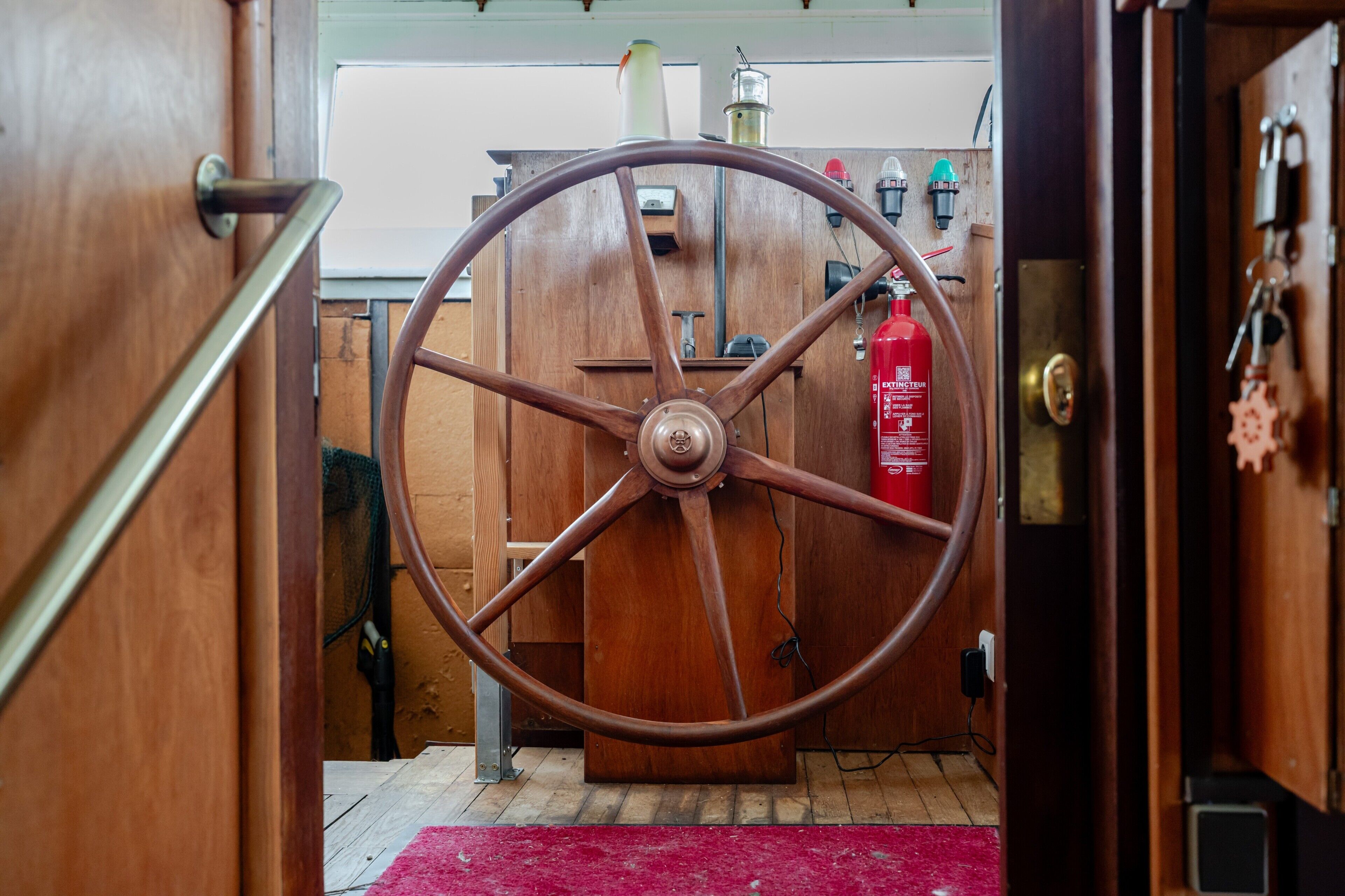 A wooden door with a large wheel handle, a red fire extinguisher, and a wooden floor.