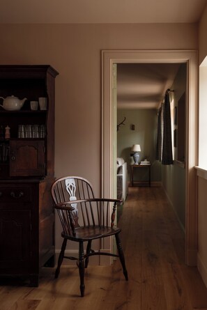 Ein Flur mit einem Holzstuhl, einem kleinen Tisch mit Lampe und einem Schrank mit Geschirr.
