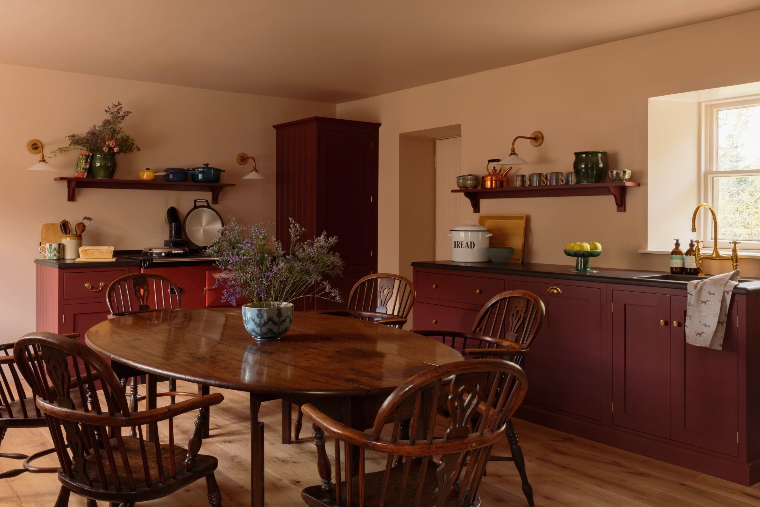 A kitchen with a wooden table and chairs, a vase of flowers, and various kitchen items on shelves.