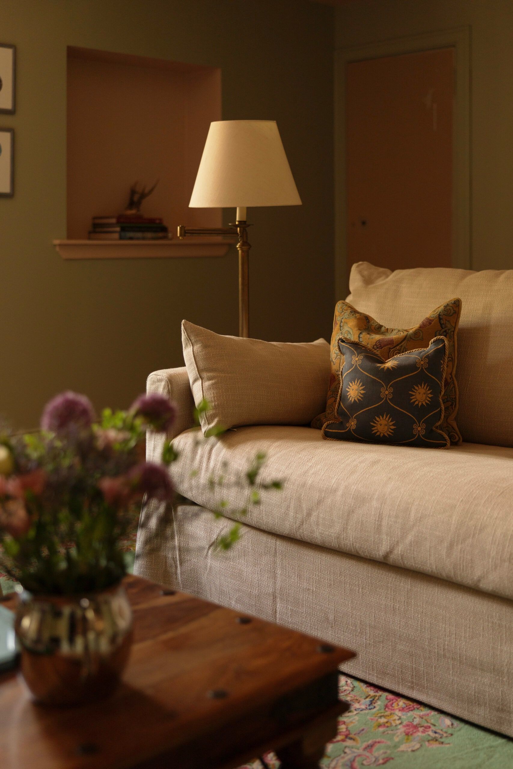 A living room with a sofa, a lamp, a small table with a vase, and a door in the background.