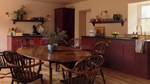 A dining room with a wooden table and chairs, a vase with flowers, and kitchen shelves with various items. - Cosy, newly renovated five bedroom cottage in the Highlands. Pet friendly! (Moy)