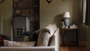 A cozy room with a stone fireplace, a sofa, a lamp, and deer antlers on the wall. - Cosy, newly renovated five bedroom cottage in the Highlands. Pet friendly! (Moy)