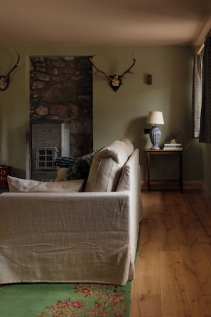 Ein gemütliches Zimmer mit Kamin aus Stein, einer Couch, einer Lampe und Hirschgeweihen an der Wand.