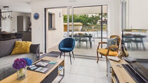 Una sala moderna con sofá, mesa de centro y sillas, un área de comedor con mesa y sillas, y una puerta corrediza de vidrio que da a un patio exterior.