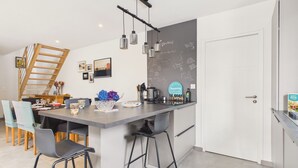 Una cocina moderna con una isla central, taburetes de bar, una escalera y una pared con una pizarra.
