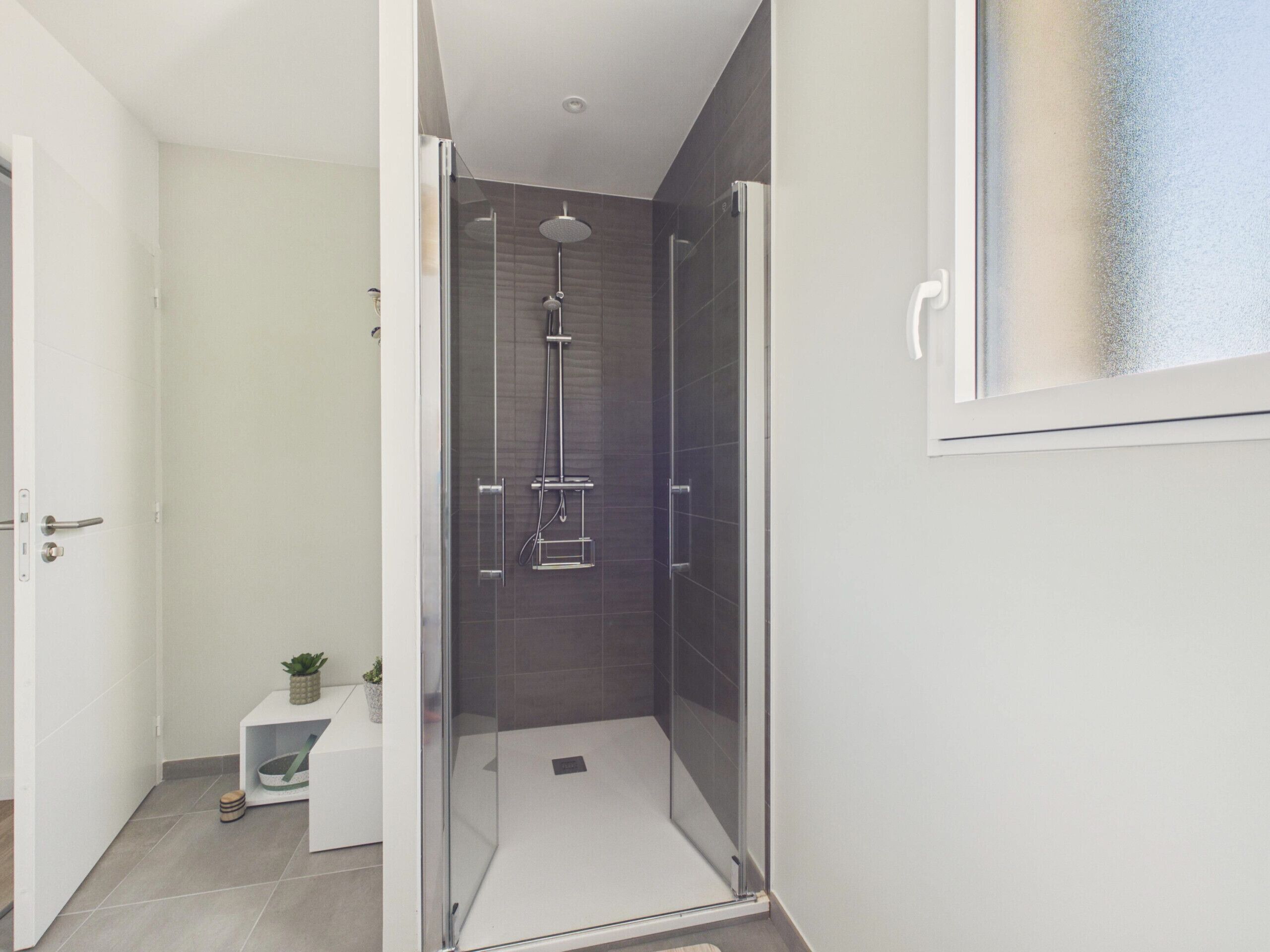 A modern bathroom with a glass-enclosed shower, a small sink area, and a potted plant.