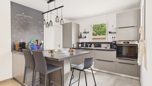Una cocina moderna con una pizarra, taburetes de bar, una mesa de comedor y un ventanal con vistas.