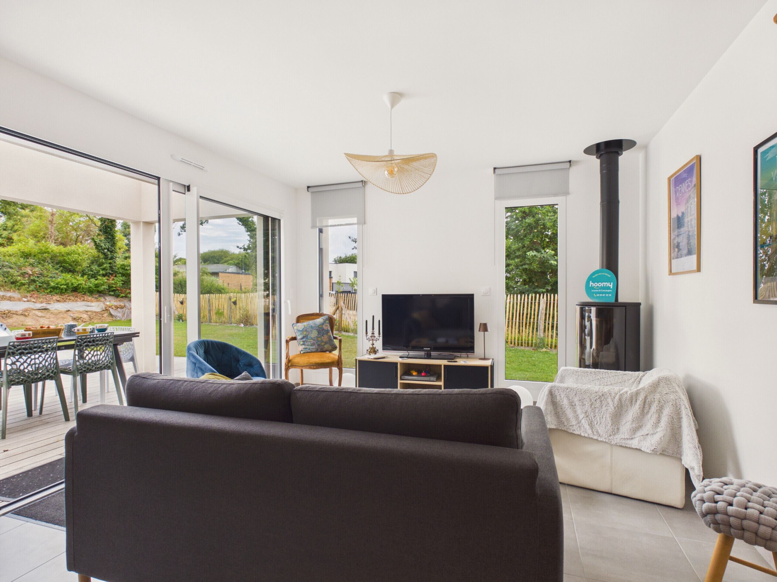 Un salon moderne avec un canapé, un téléviseur et une cheminée, de grandes fenêtres et un coin repas offrant une vue sur l’extérieur.