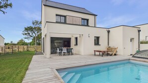Una casa moderna de dos pisos con piscina, un patio con mobiliario exterior y un patio cercado.