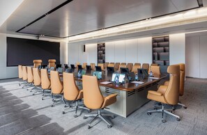 Un salón de conferencias con una larga mesa, varias sillas, computadoras portátiles y una pantalla grande.