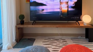 Un téléviseur posé sur un meuble en bois, une petite plante en pot et une lampe sur une table de chevet.