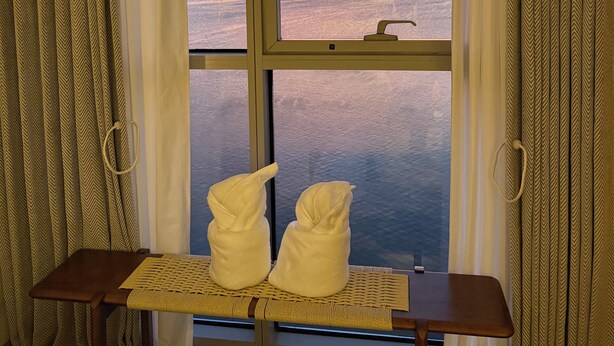 Une pièce dotée d’une grande fenêtre, d’une petite table avec des serviettes et de rideaux.