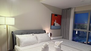Une chambre d’hôtel avec un lit, une lampe, un tableau et une fenêtre donnant sur la ville.